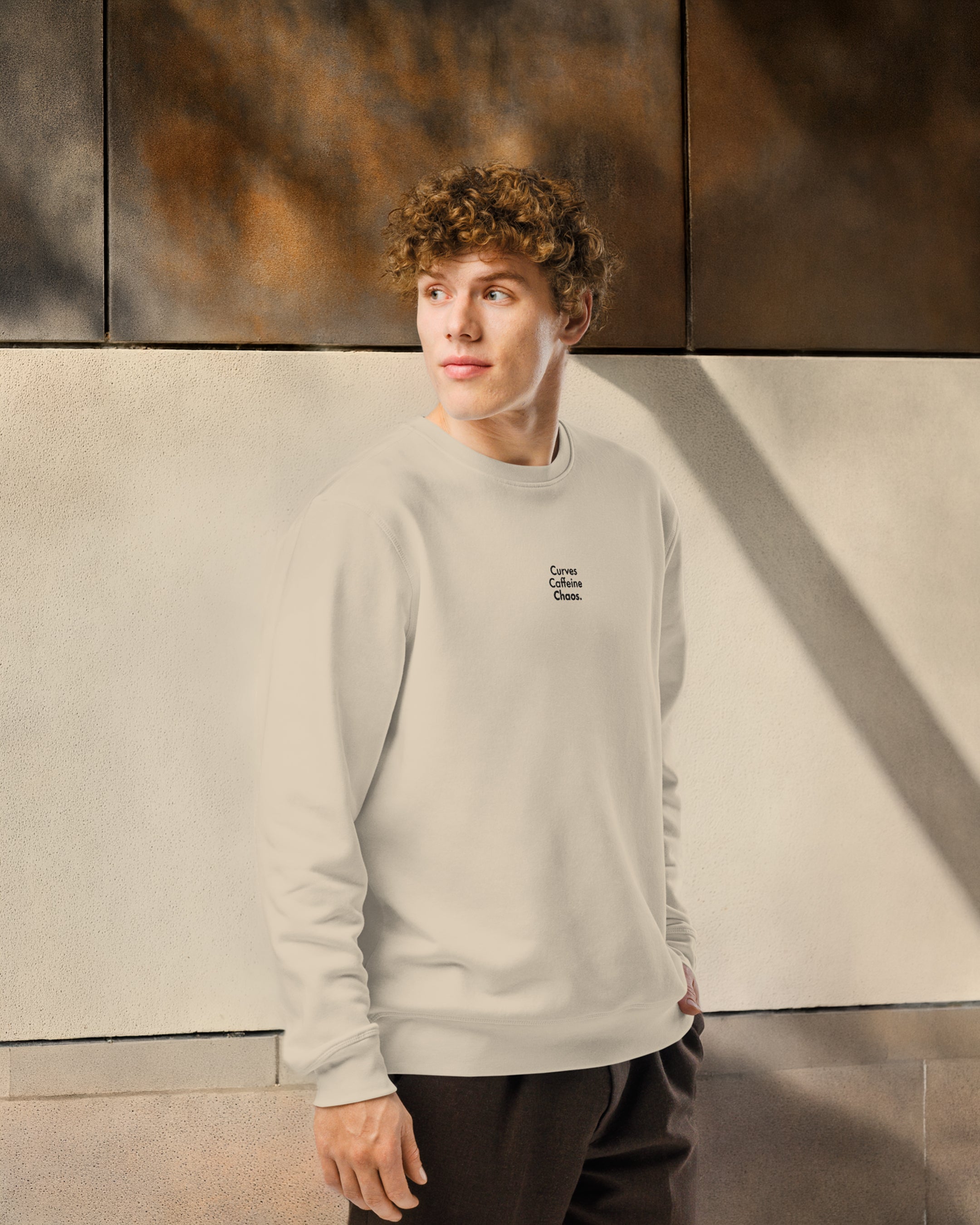 Person wearing a light beige sweatshirt with text, standing against a textured wall.