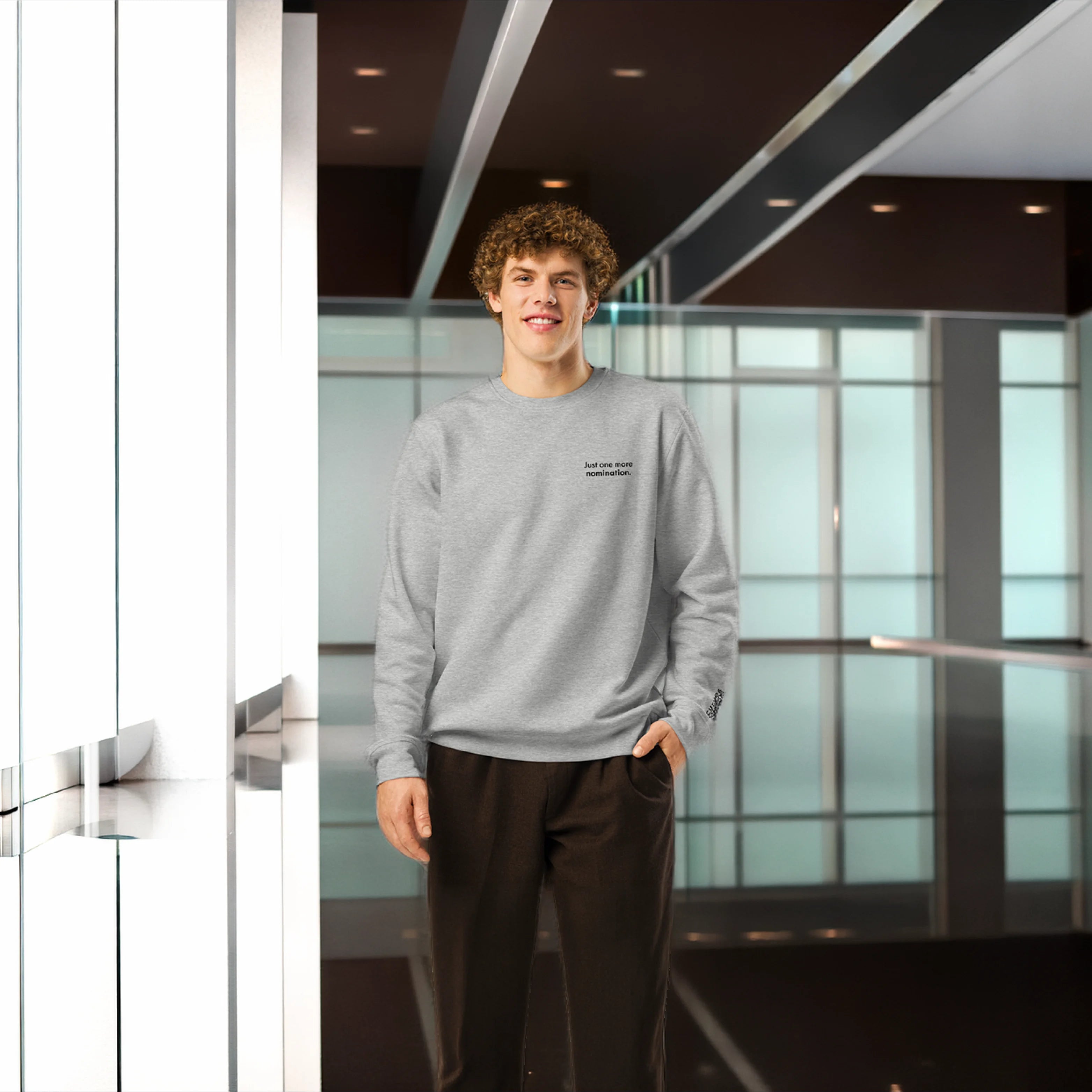 Person wearing a gray sweatshirt standing in a modern indoor setting with glass walls.